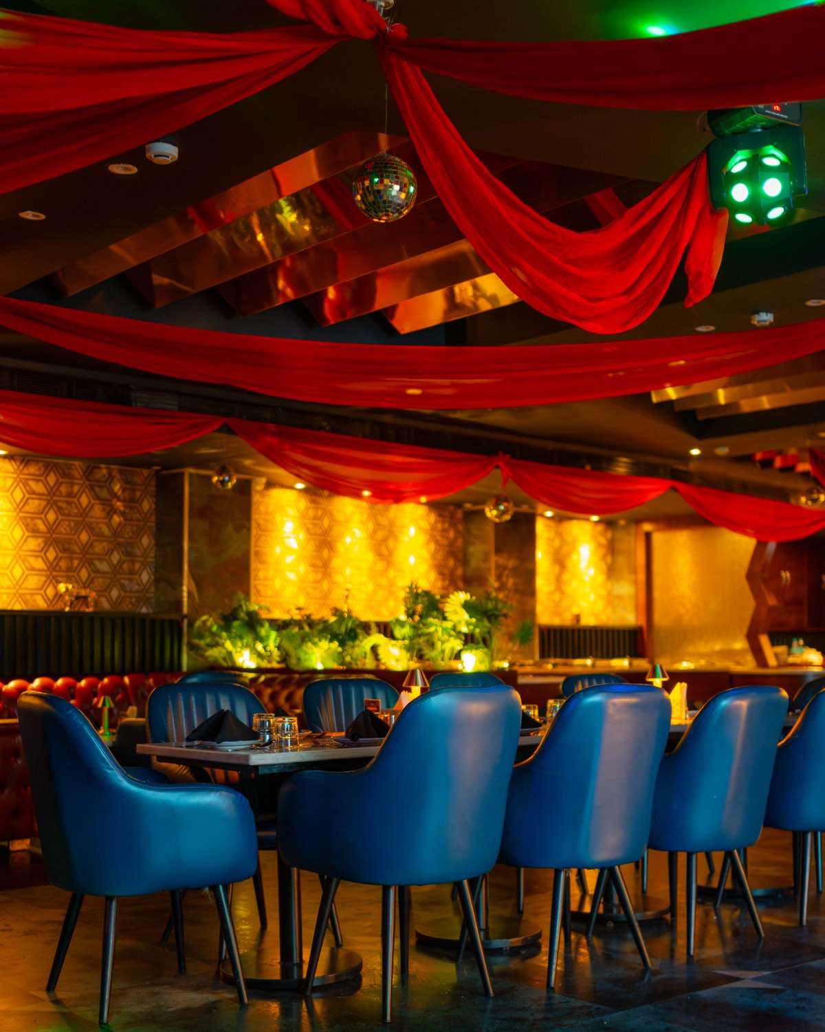 Bellers dressed for a party, red drapes across the ceiling, a disco ball and blue chairs at the tables