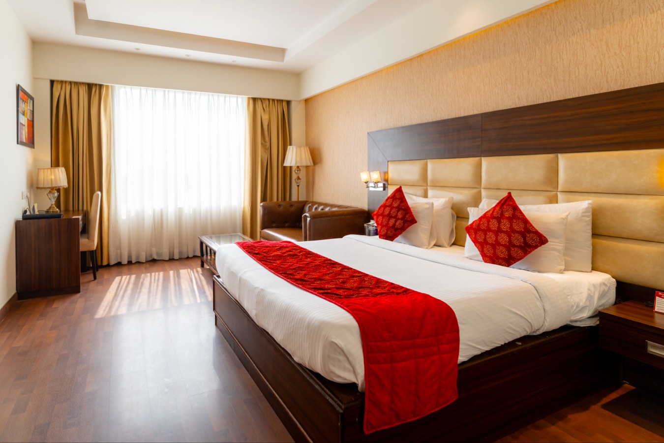 An Executive Room in daylight, the king bed with its red runner and the leather sofa by the window