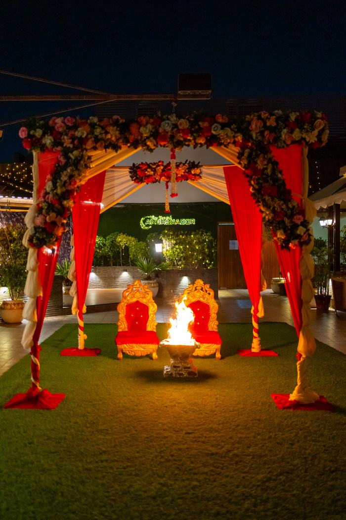 A floral mandap with two thrones, lit after dark