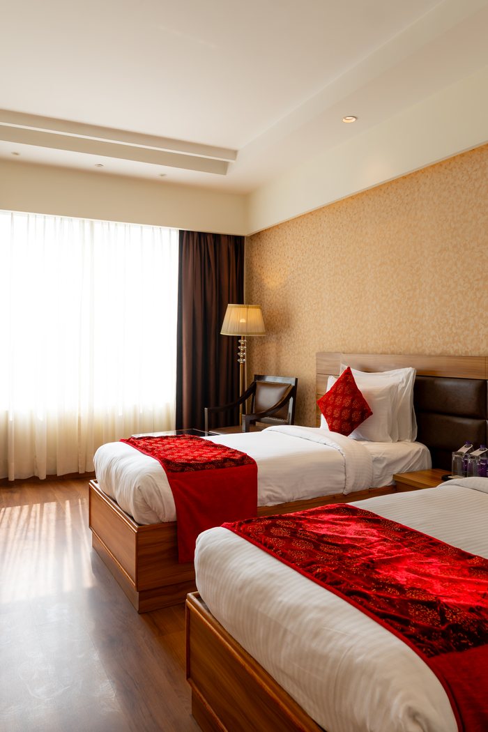 A twin room in daylight, two beds made up with red runners