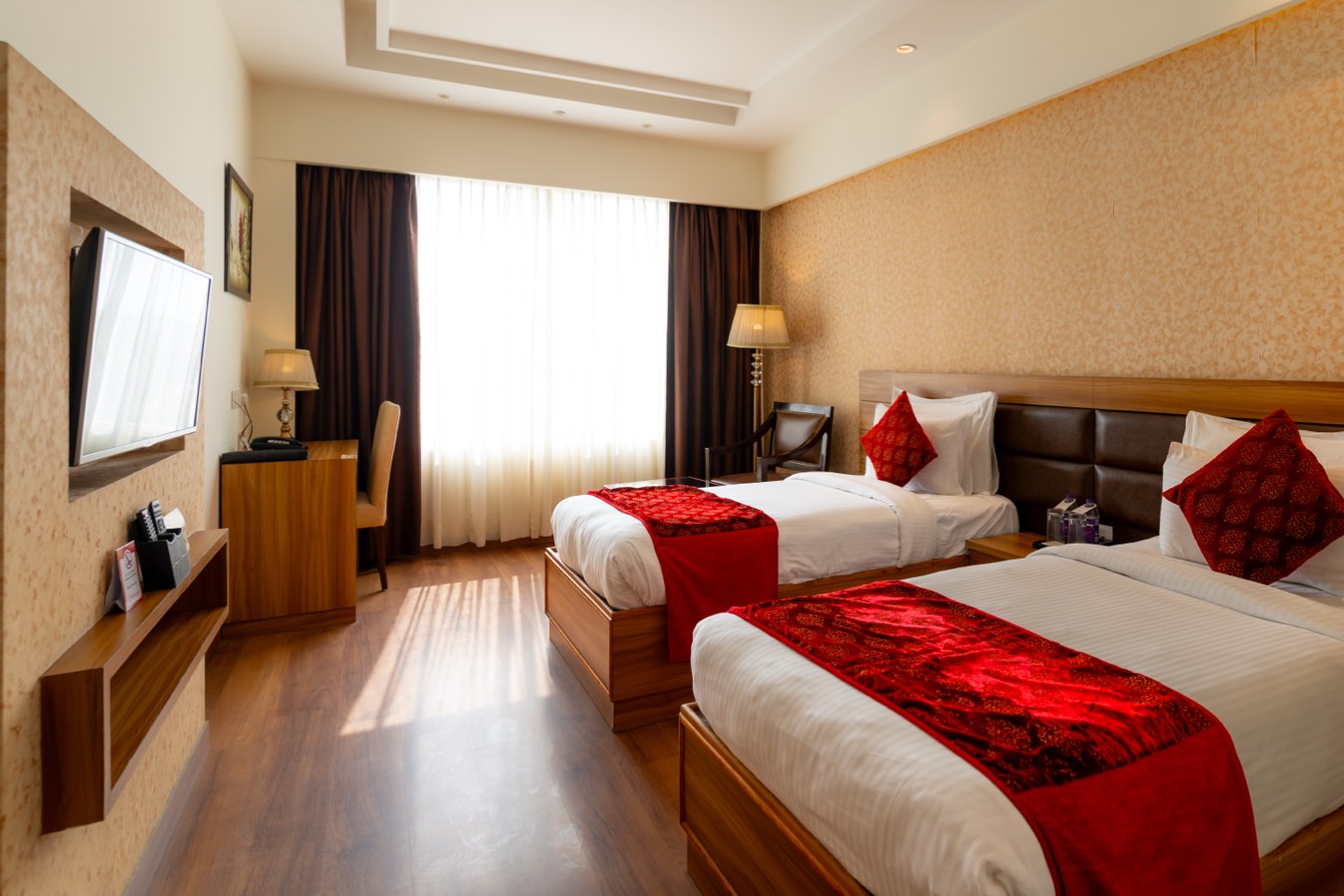 A Twin Room in daylight: two single beds with red runners, the television on the wall and the sun across the floor